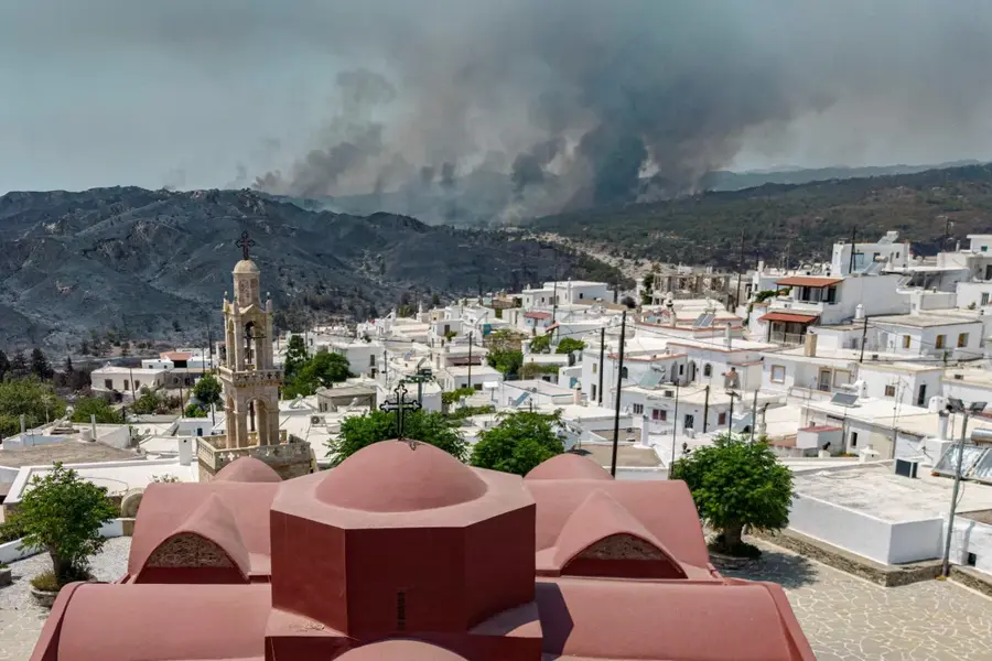 A view of the village of Asklipieio, as a wildfire burns in the background, on the island of Rhodes, Greece, on July 26. [Nicolas Economou/Reuters]