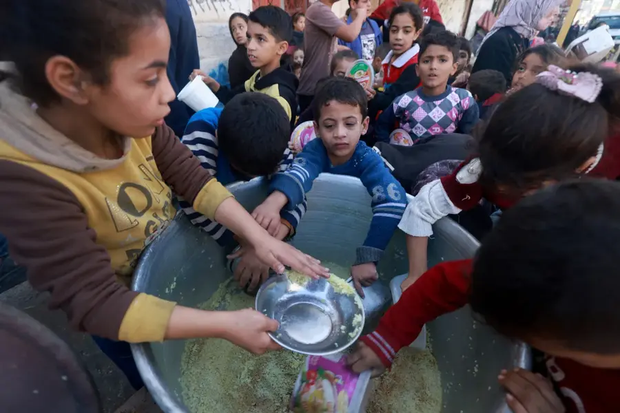 Palestinian children collect food at a donation point provided by a charity group in the southern city of Rafah on December 6, 2023. [Mohammed Abed/AFP]