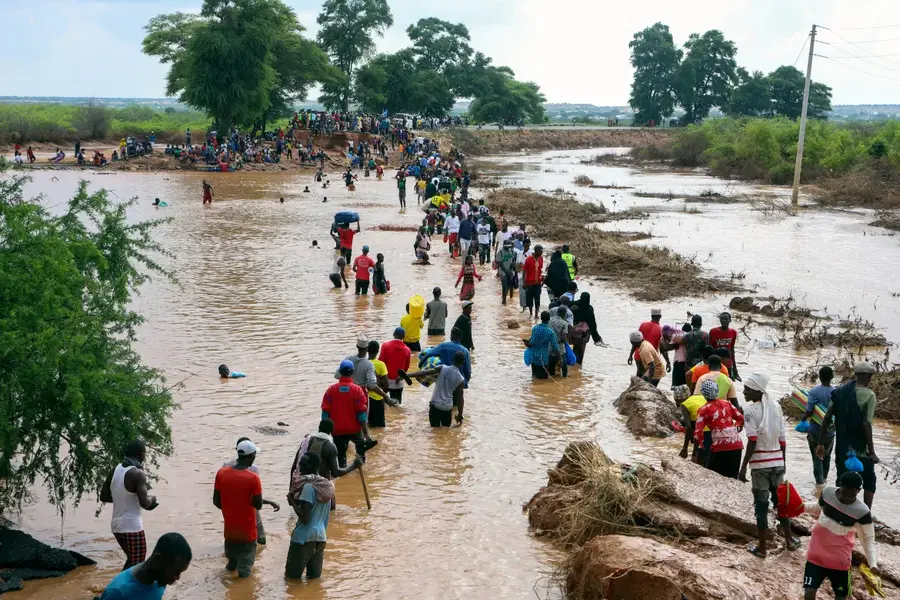 People wade through floodwaters after a section of road was destroyed in Mororo, North Eastern Kenya, on November 30, 2023. [AP Photo]