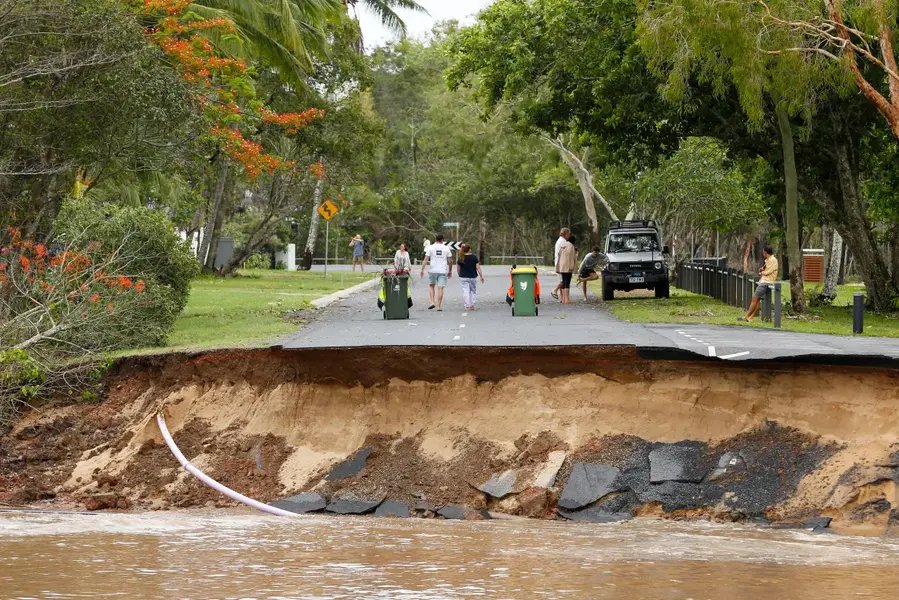 Stranded residents stand on a road, a large section of which has washed away, in the suburb of Holloways Beach in Cairns, Australia, on December 18, 2023. [Joshua Prieto/AAP Image via AP]